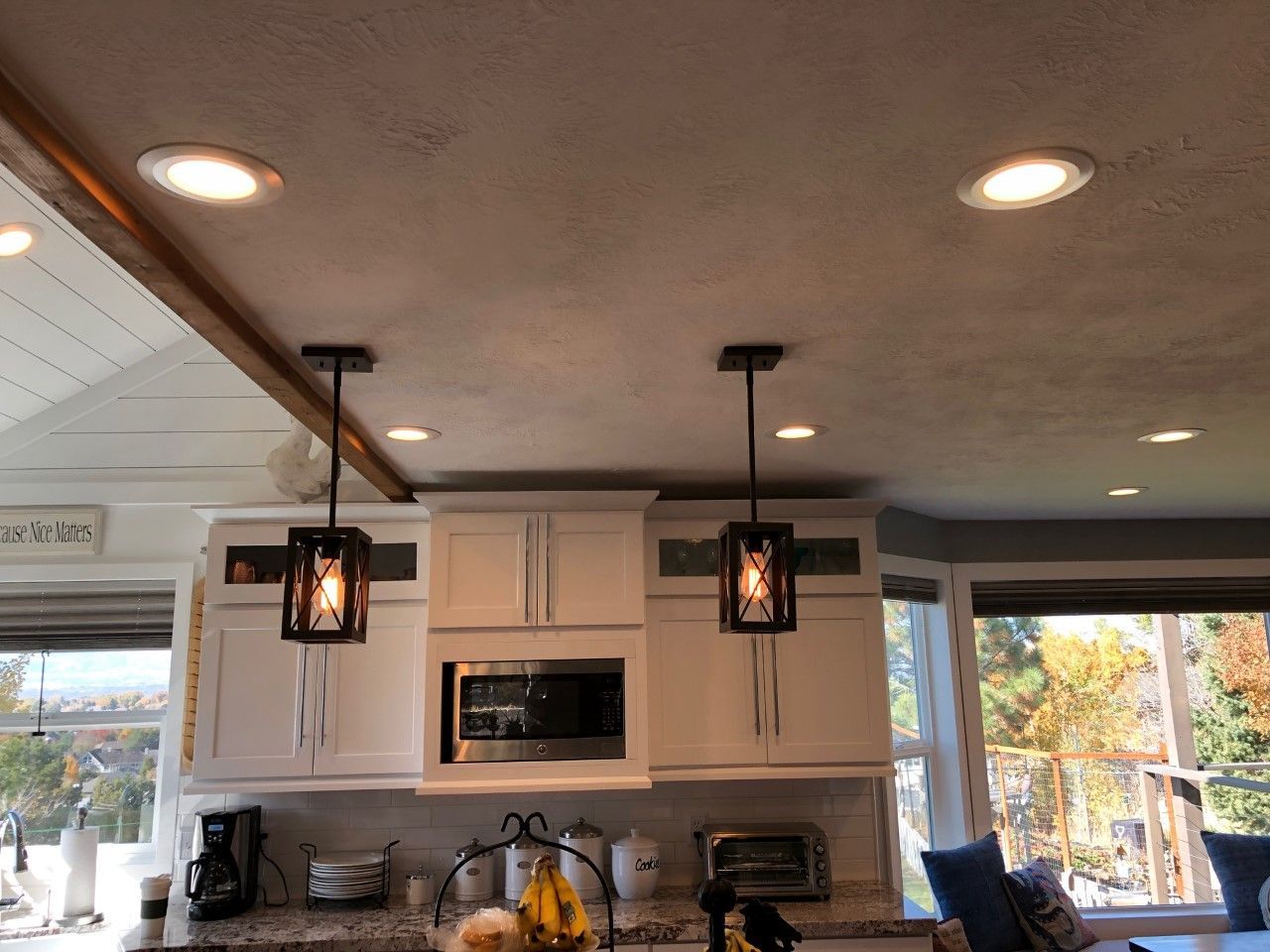 Modern kitchen with white cabinets, pendant lights, recessed ceiling lights, and large windows overlooking trees