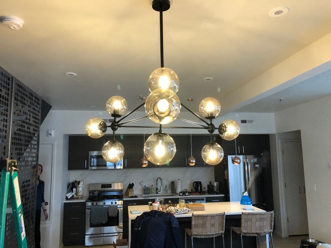 Modern kitchen with a large black chandelier, island seating, and stainless-steel appliances