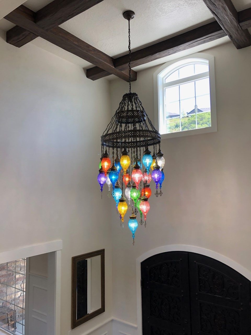 Colorful chandelier-style pendant light hanging in a foyer with white walls and a window.