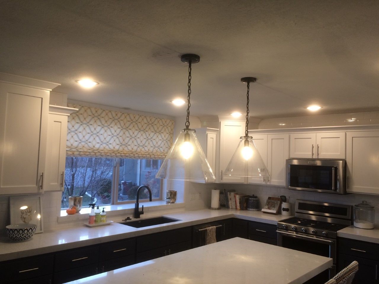 Modern kitchen with white cabinets, black countertops, pendant lights, and a large window over the sink
