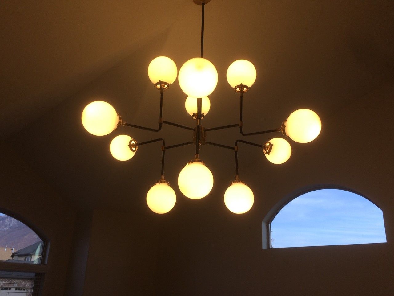 Ceiling chandelier with glowing round bulbs in a dim room, seen above arched windows