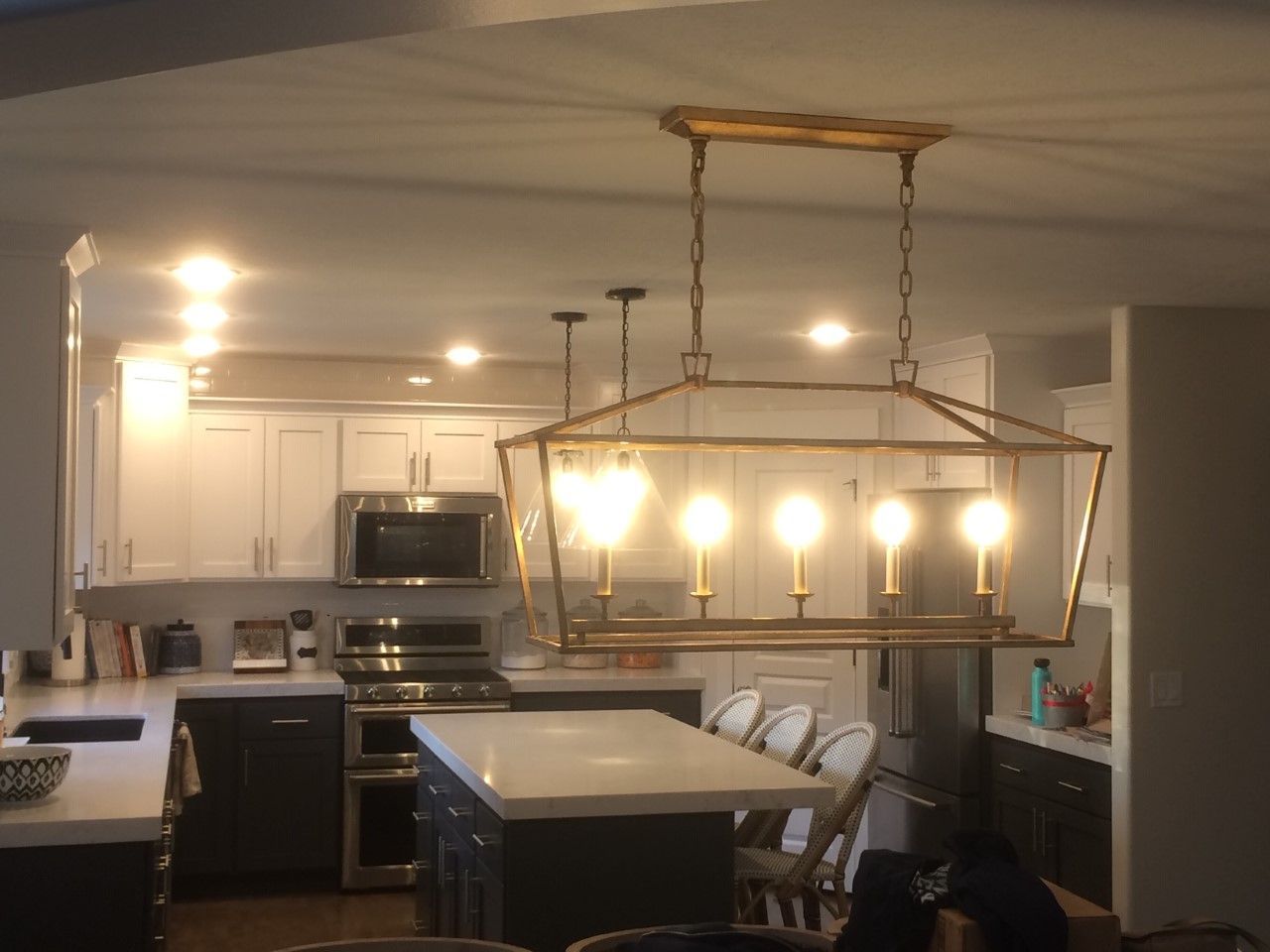 Modern kitchen with white cabinets, black appliances, central island, and hanging chandelier over dining area
