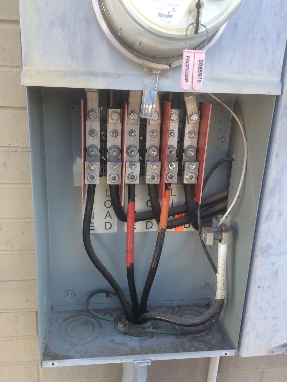 Open electrical meter box with exposed wiring and circuit breakers inside a gray panel.