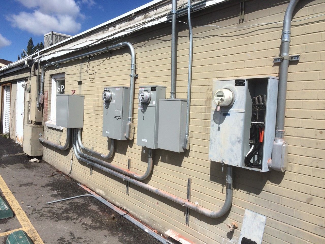 Exterior wall with multiple gray electrical meter boxes and conduit on a beige brick building.