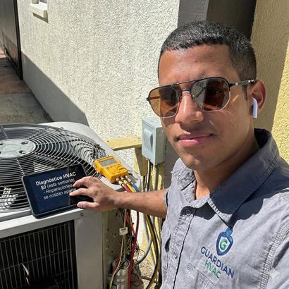 Technician pressure-washing an outdoor air conditioner unit beside a house