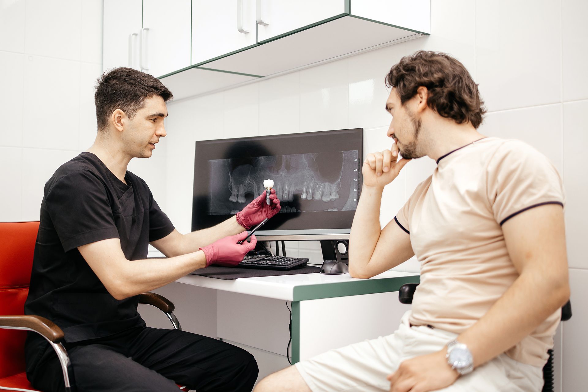 Dentist explaining dental implant treatment to a patient with an implant model and X-ray