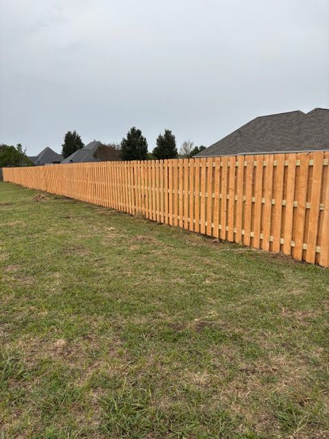 Wooden fence in a grassy yard, with houses and trees in the background under an overcast sky.