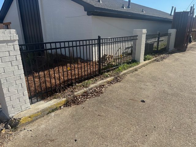 Black metal fence with brick and concrete pillars, next to a building and an alley.