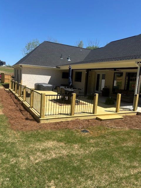Wooden deck with black railings and light wood posts attached to a house with a black roof.