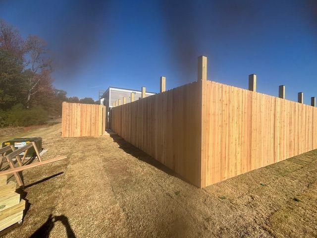 Wooden fence under construction on a grassy area, with clear blue sky in the background.