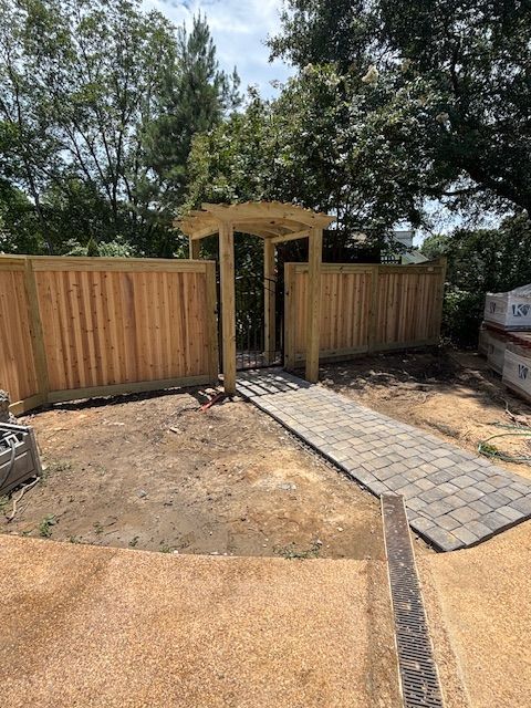 Wooden fence with gate, walkway, and arbor in a yard.