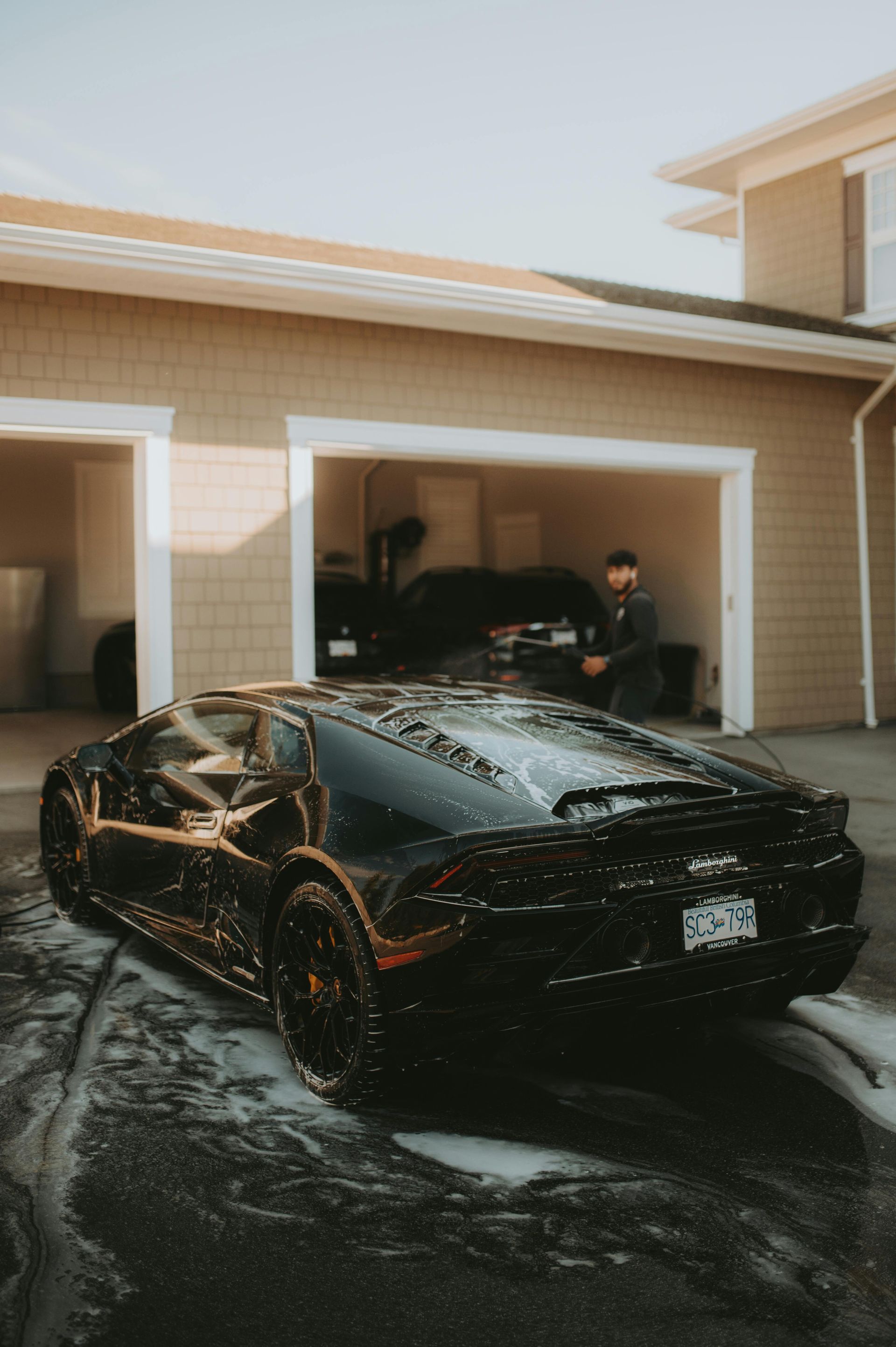 Black Lamborghini being washed outside a tan garage; a person stands inside.
