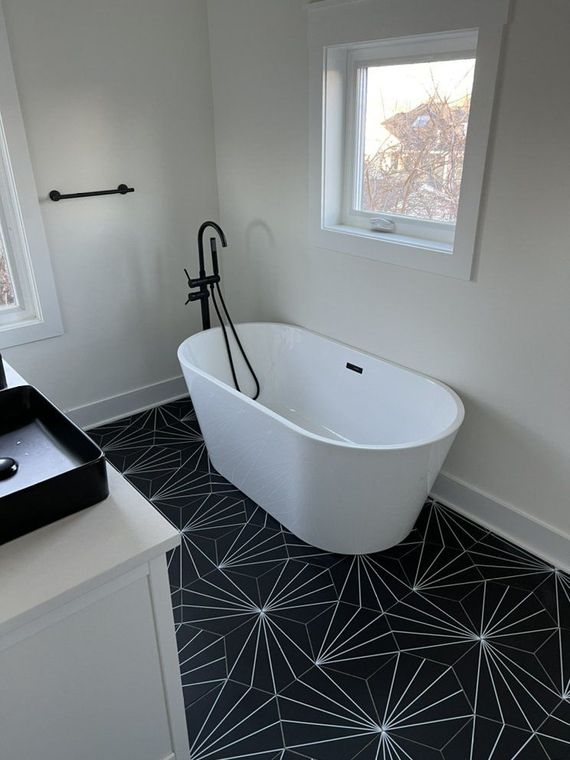 Modern bathroom with black and white geometric tiled floor, white soaking tub, and black fixtures.