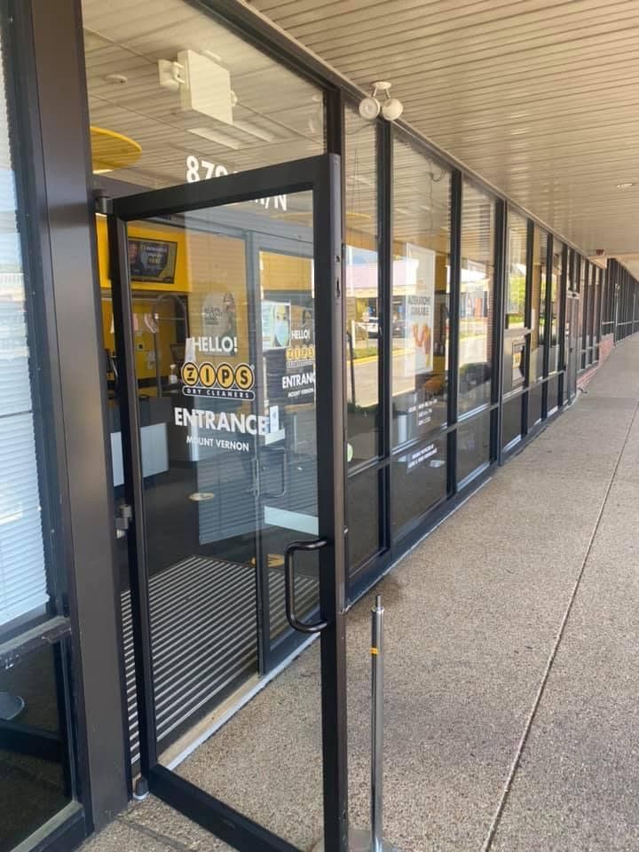Entrance to a business with a glass door and windows in a strip mall. The sign reads
