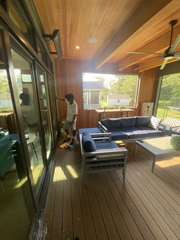 An outdoor living area with a young person standing near a sliding glass door. There are blue couches and a wooden ceiling.