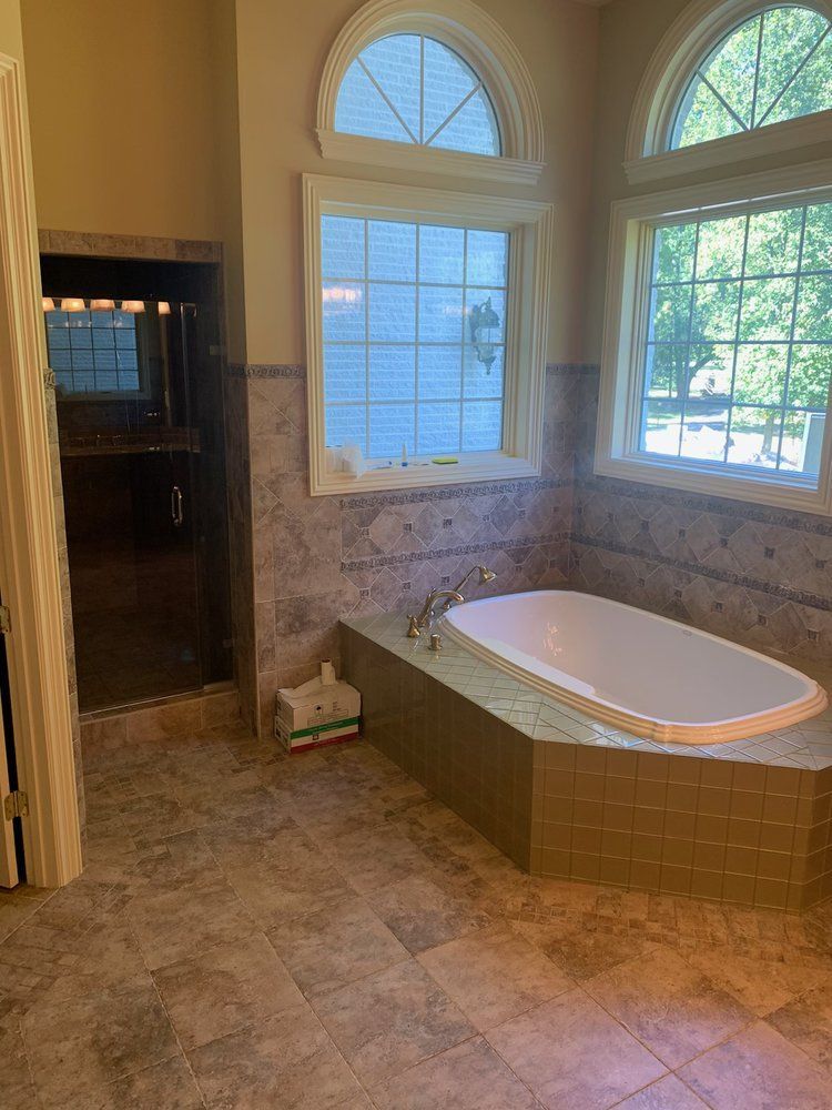 Spacious bathroom with a bathtub and shower. The walls are tiled, and two arched windows offer natural light.