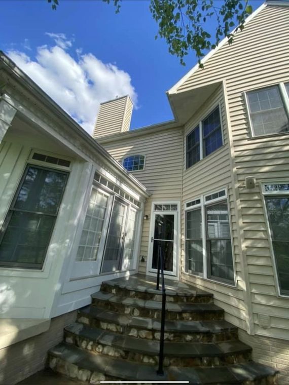Exterior of a light beige house with multiple windows and a stone staircase leading to a black door. Bright blue sky.