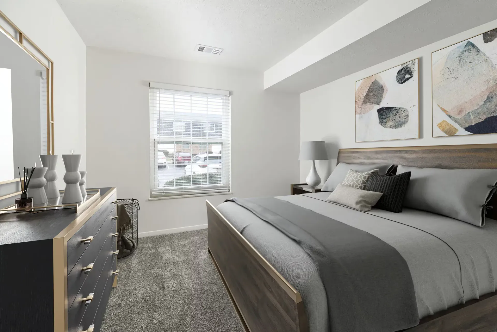 Bright apartment bedroom with a gray bed, dresser, nightstand, window blinds, and abstract wall art.