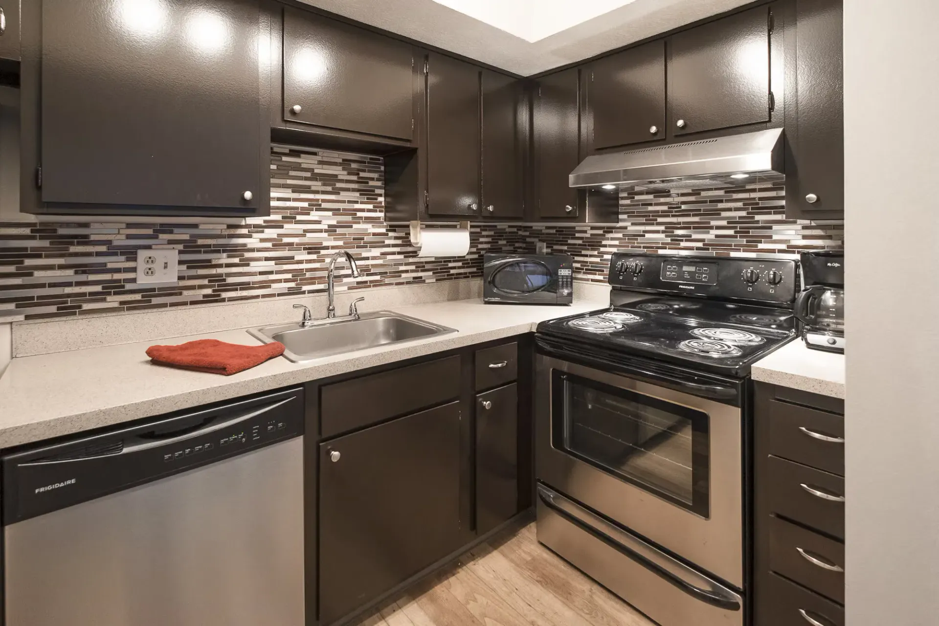 U-shaped kitchen with dark cabinets, stainless steel appliances, and a mosaic tile backsplash.