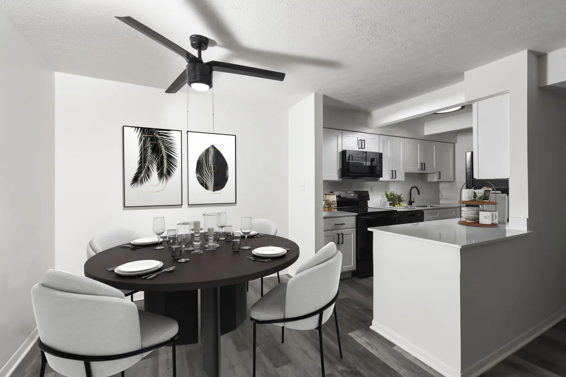 Open-concept dining area with round dark table and light upholstered chairs beside a white kitchen.