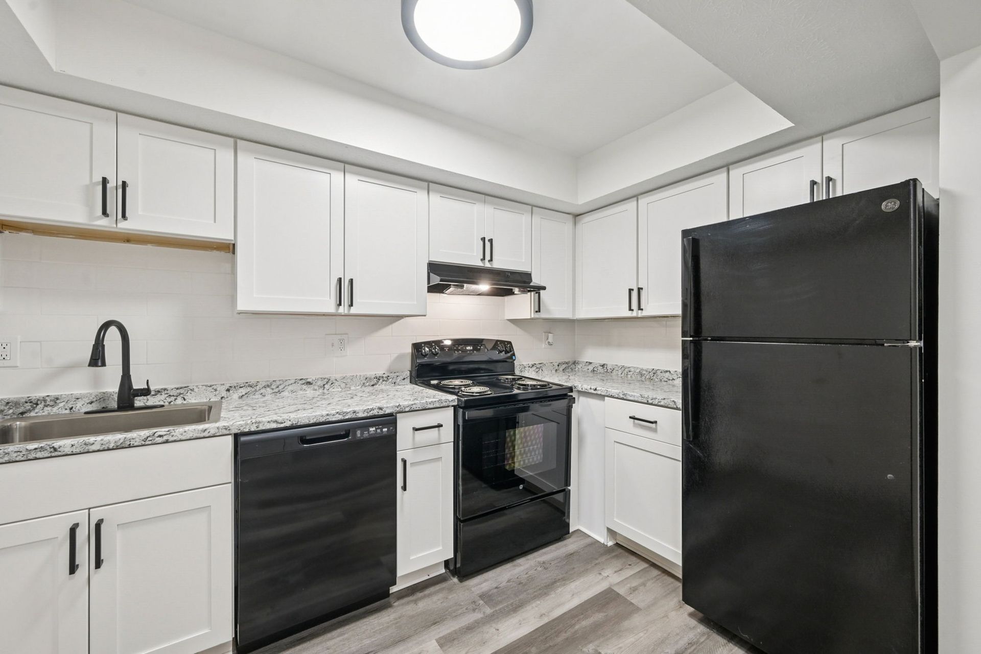 Modern kitchen in an apartment with white cabinets, black appliances, granite countertops, and a stainless steel sink.