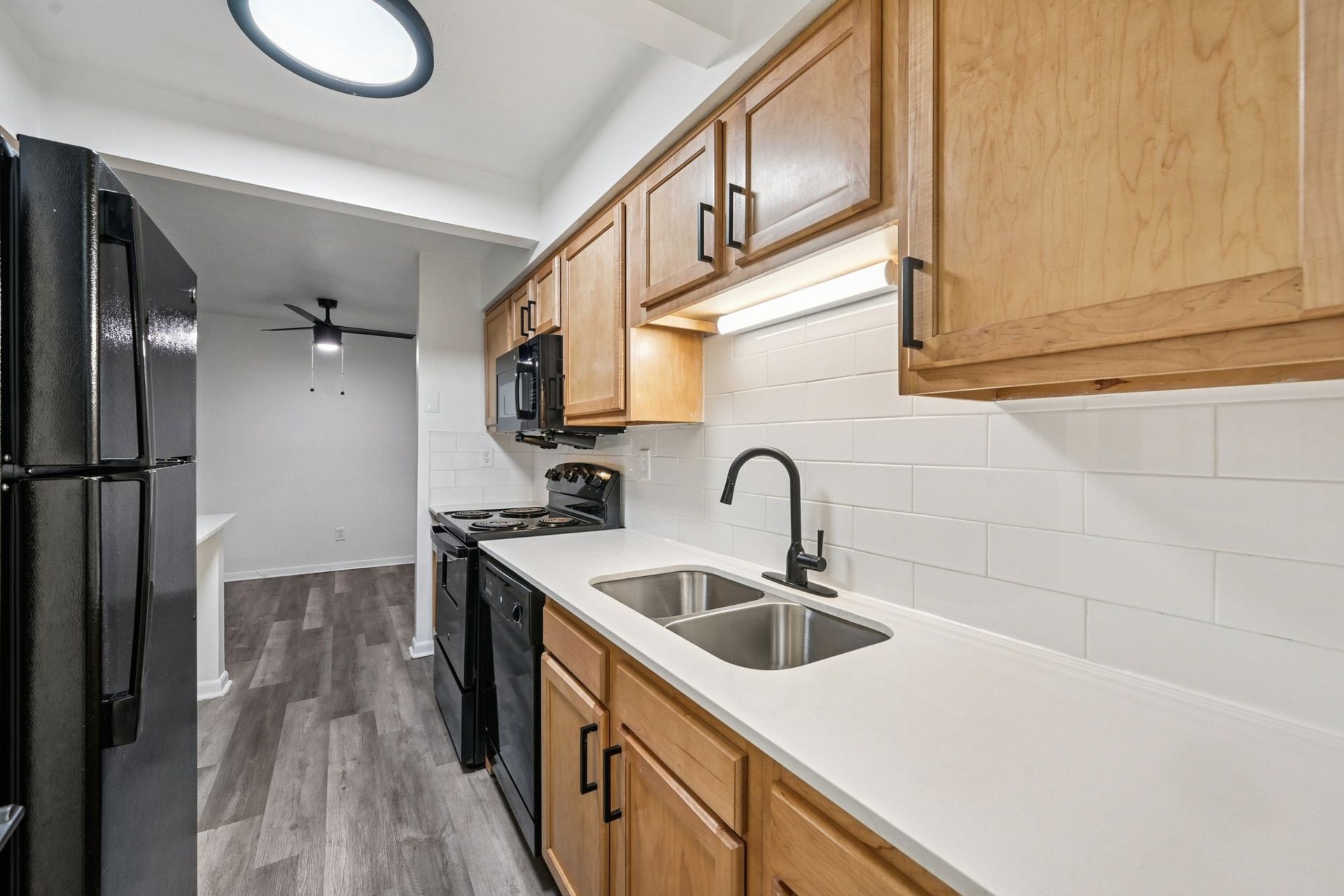 Kitchen in an apartment with white counters, white subway tile backsplash, wooden cabinets, and black appliances.