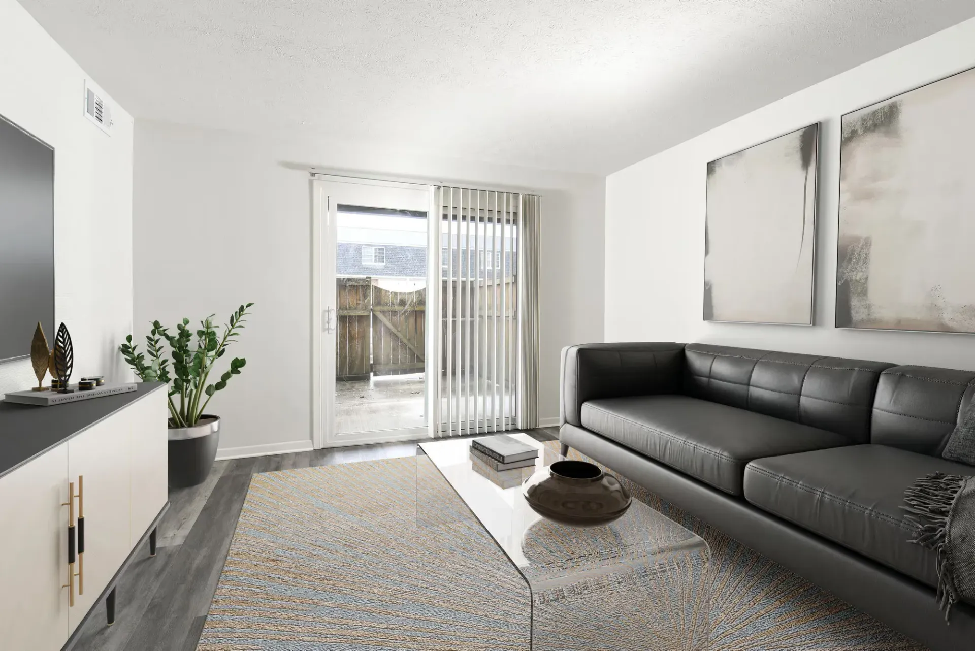 Living room in an apartment with a black leather sofa, glass coffee table, and sliding door with blinds.