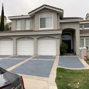 Two-story stucco house with three-car garage, blue driveway, and green lawn.
