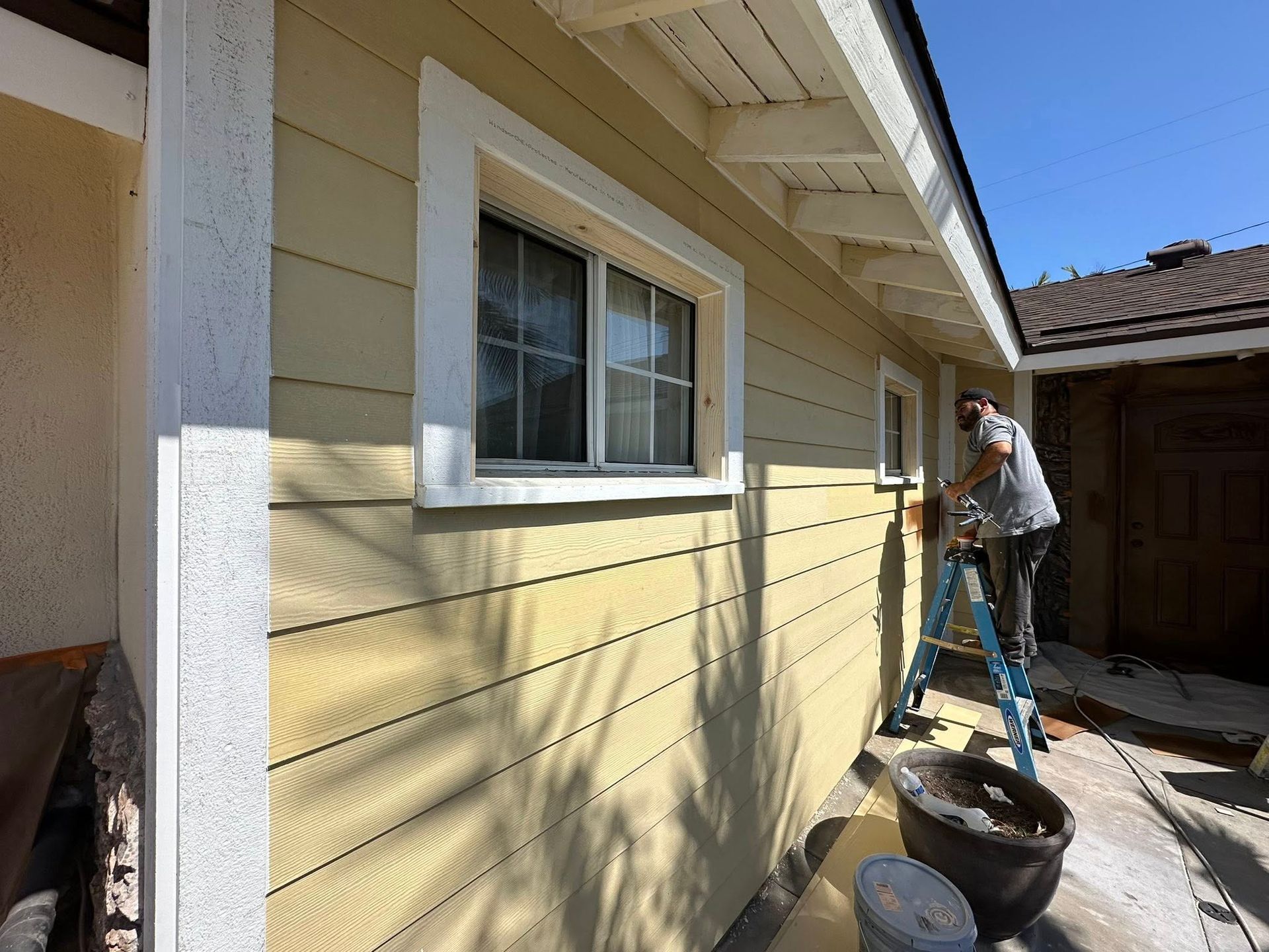 Person painting exterior yellow house trim near window.
