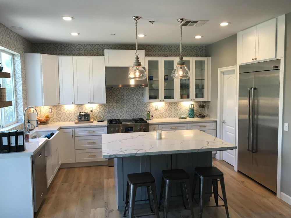 Modern kitchen with white cabinets, gray island, stainless steel appliances, pendant lights.