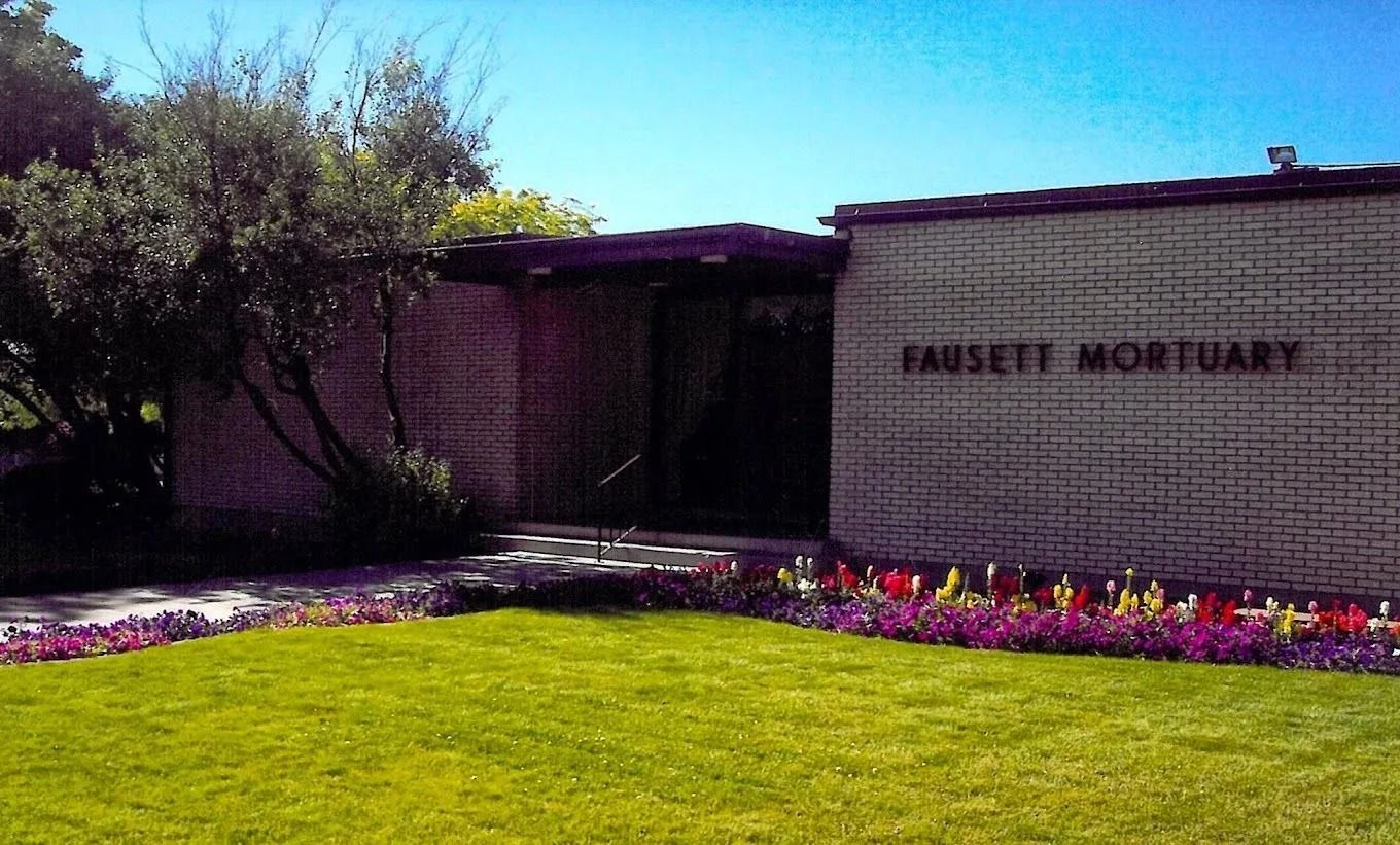 Manicured lawn and flowerbed beside a brick building with a sign reading “Moseley Mortuary”