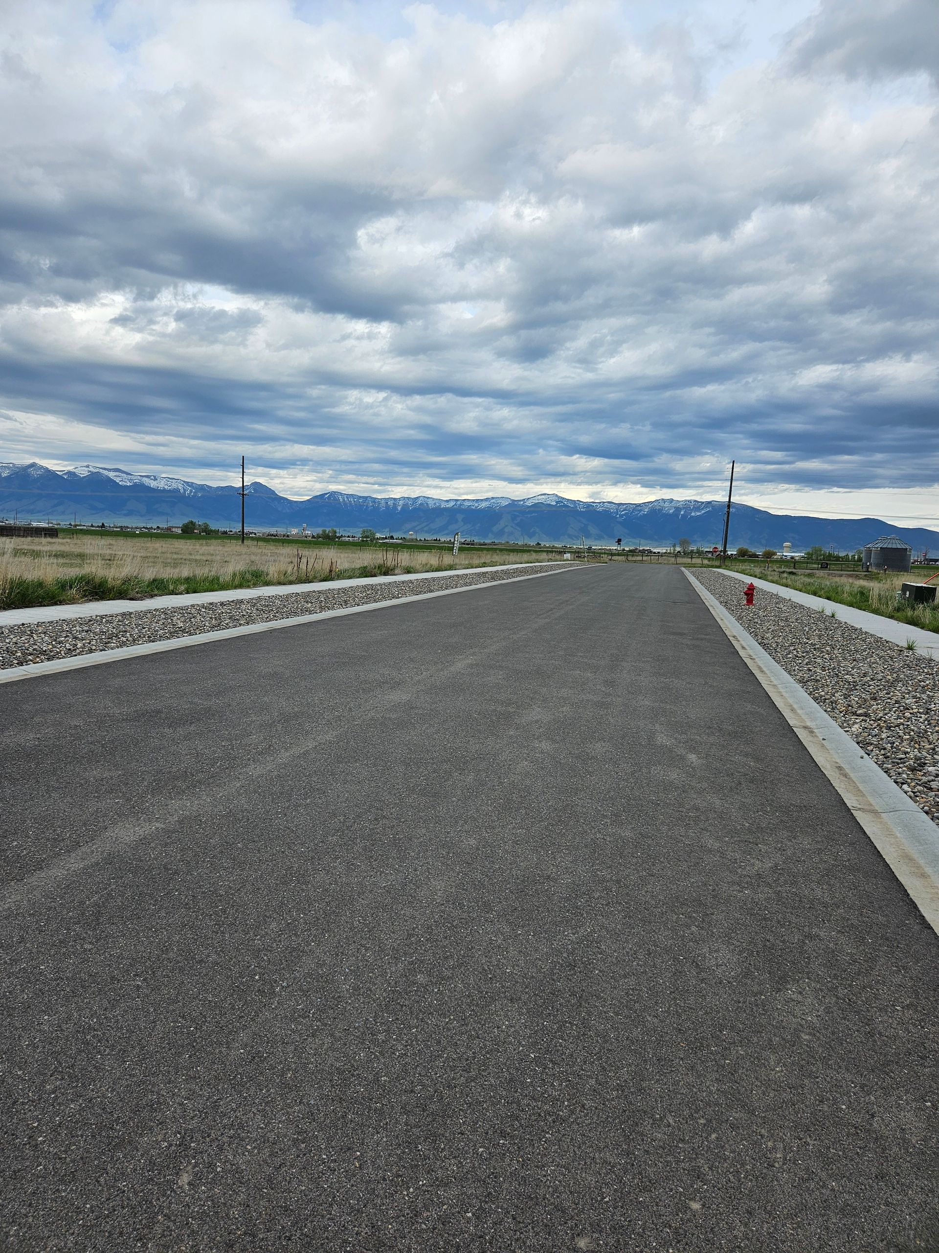 Paved path bordered by rocks and vegetation, leading toward mountains under a cloudy sky.