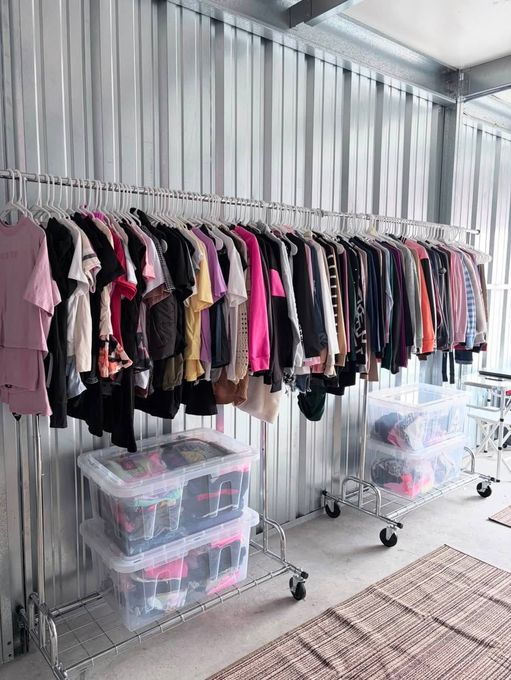 Clothing rack with assorted tops and pants, plus clear storage bins in a bright room