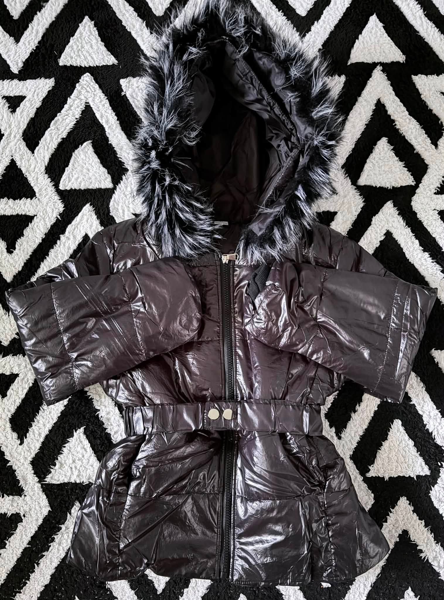 Black puffer coat with hood and belt laid flat on a black-and-white patterned rug