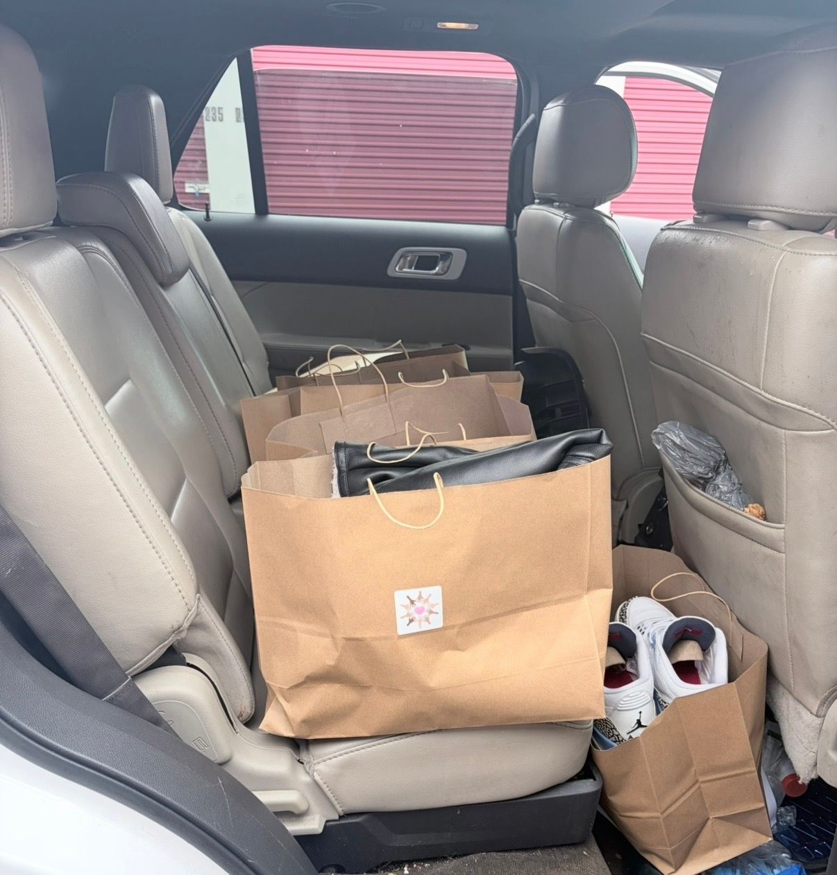 Paper shopping bags and a pair of shoes on the back seat of a car.