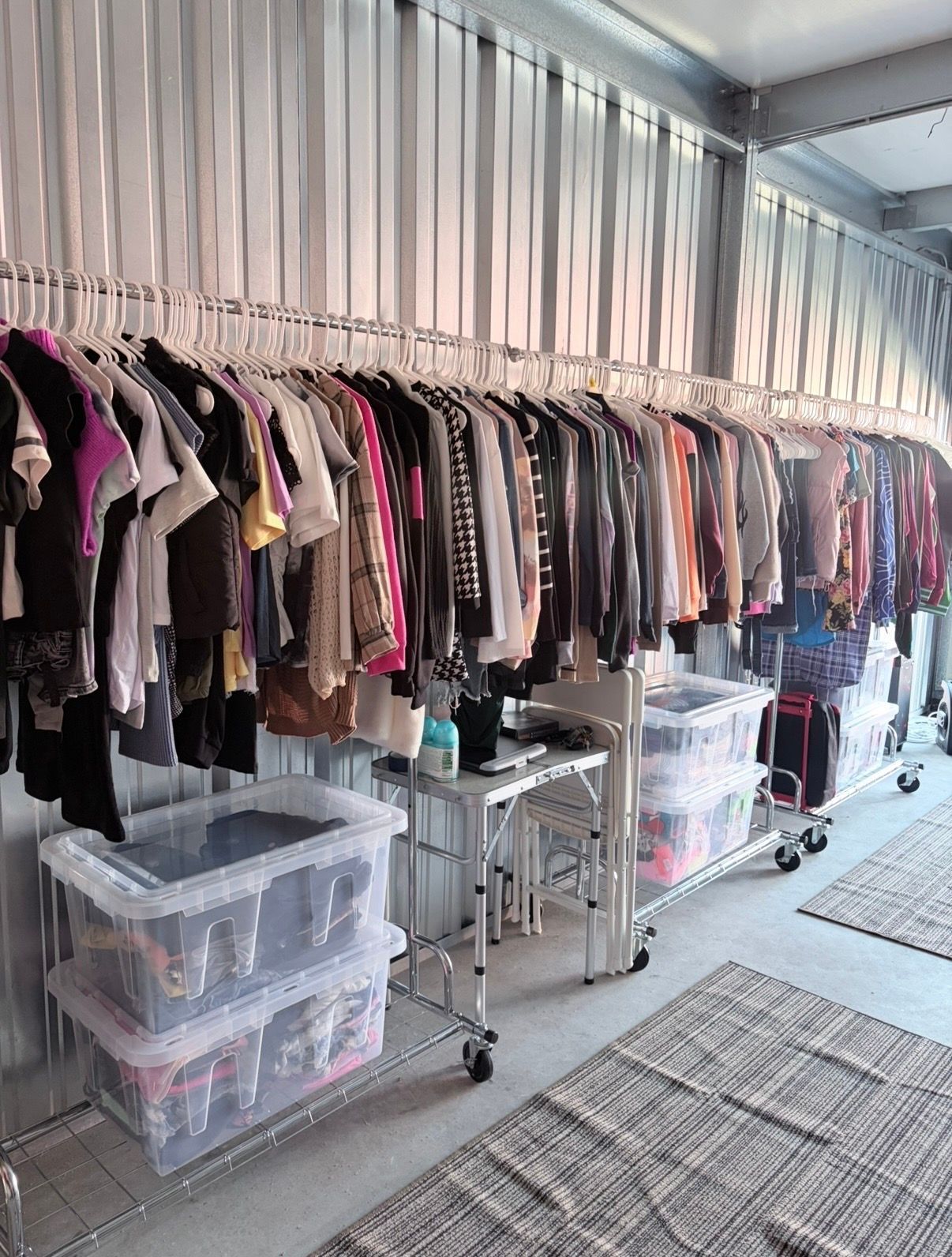 Racks of assorted clothes in a bright boutique with clear storage bins and a narrow aisle