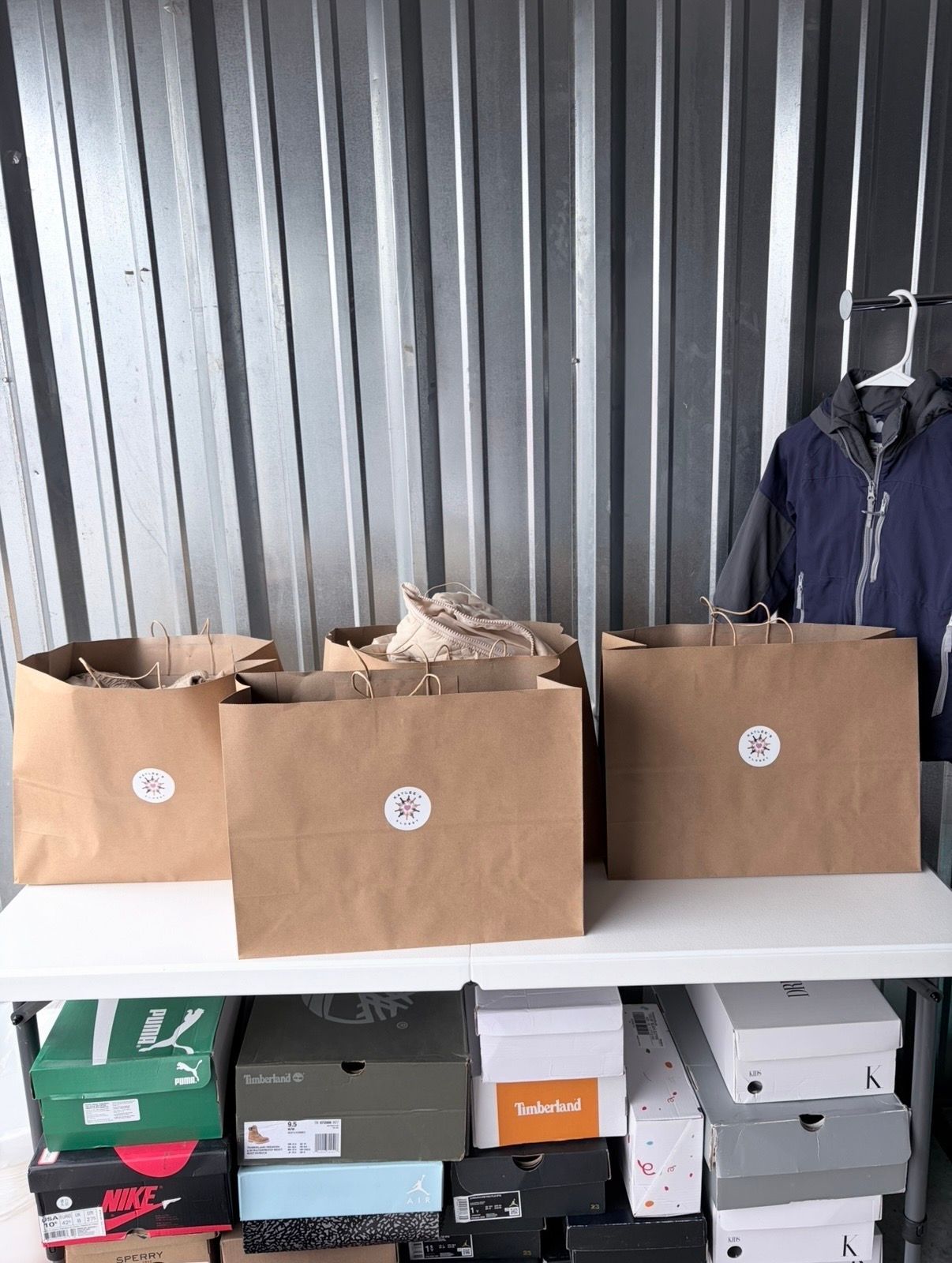 Three brown paper bags on a shelf beside a hanging dark jacket, with shoe boxes stored below.