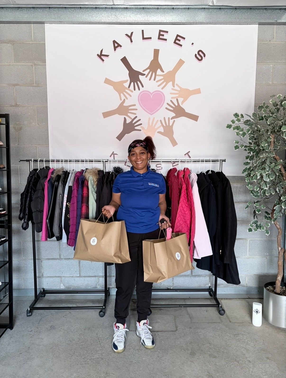 Person holding shopping bags in front of a clothing rack display with the “Kaylee’s” logo.
