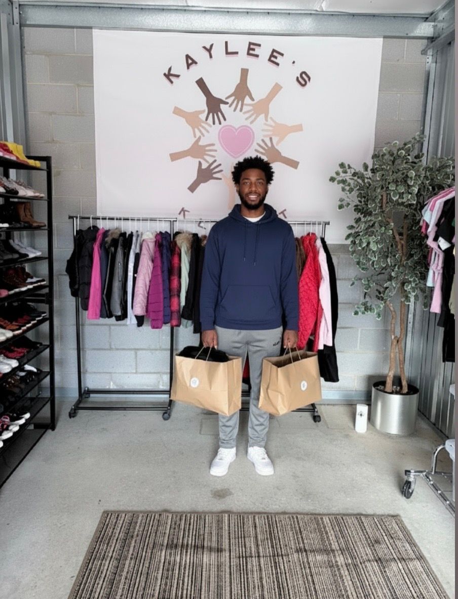 Man holding two tan shopping bags in a boutique with clothing racks and a 
