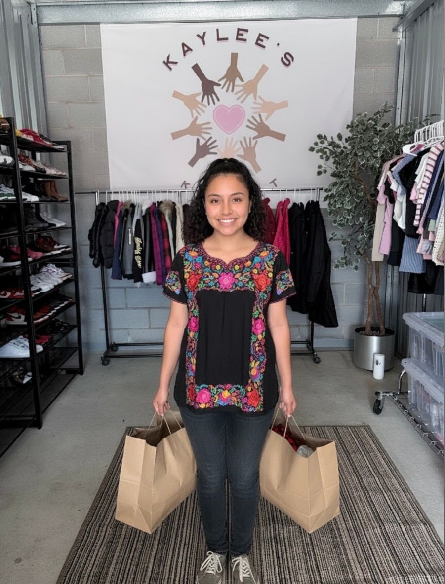 Woman in a clothing boutique holding two shopping bags, standing and smiling amid racks of clothes.