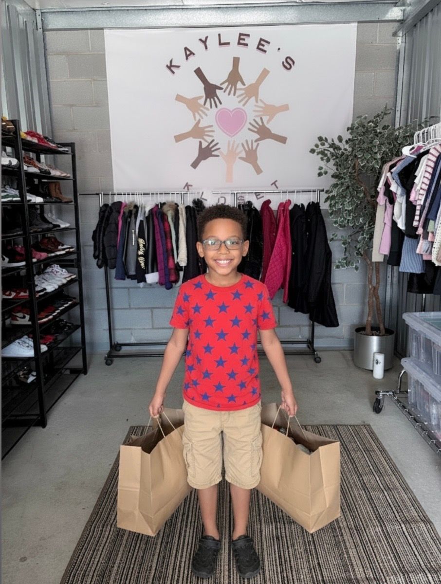 Child standing in a clothing boutique with shopping bags and racks of clothes behind them