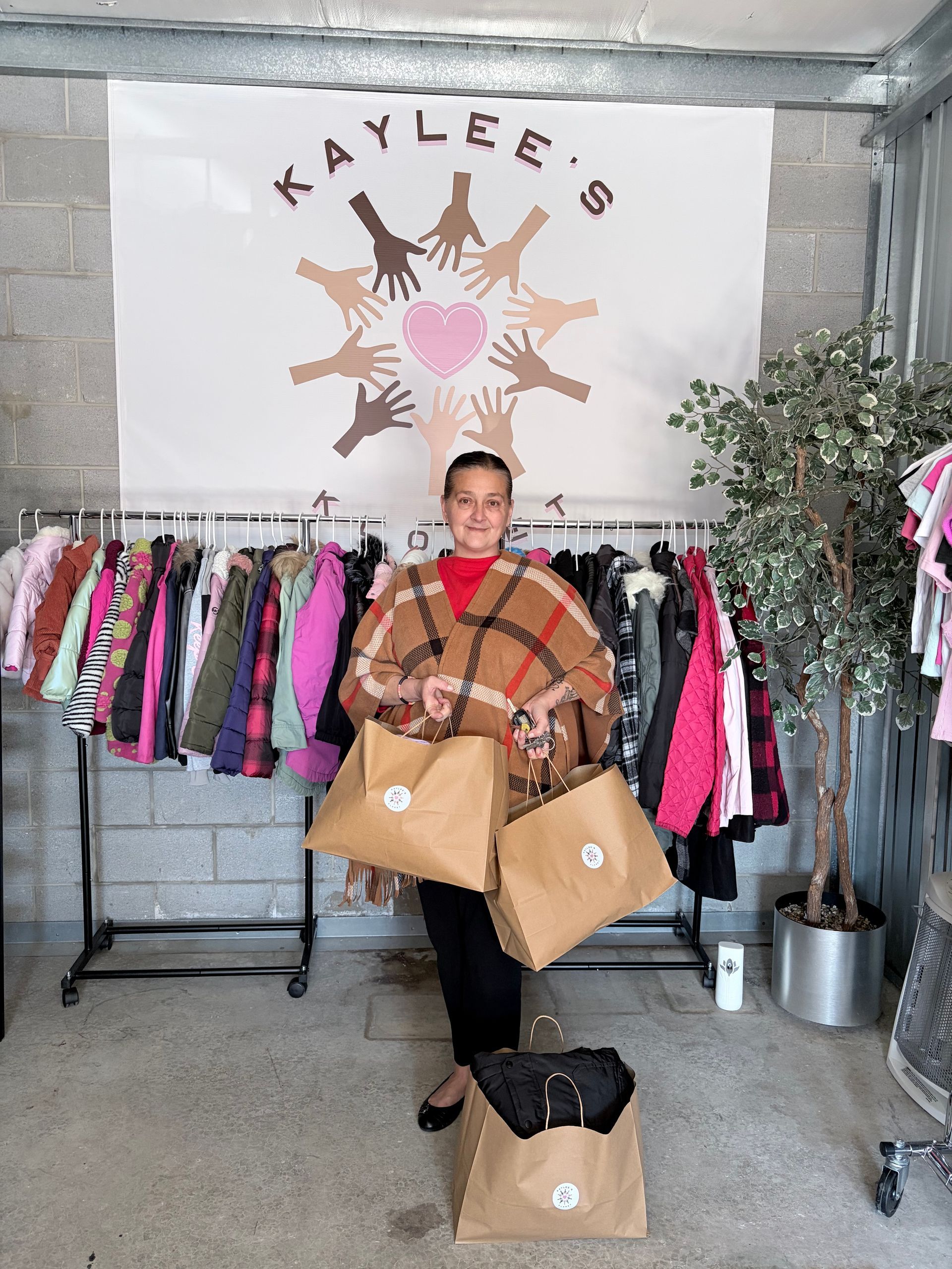 Person holding shopping bags in front of a clothing rack under a “KAYLEE’S” sign.