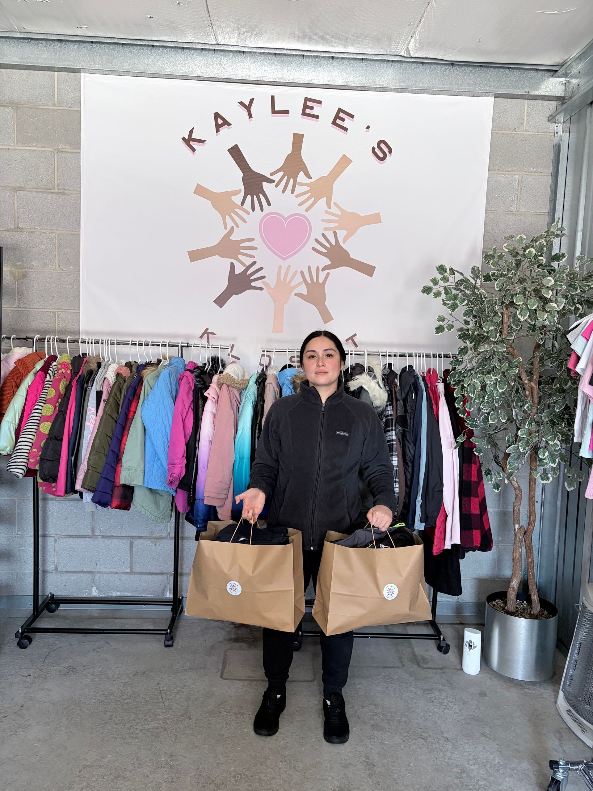 Person holding two shopping bags in front of a clothing rack under a 