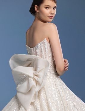 Woman in a strapless white wedding dress with a large bow detail. Blue background.