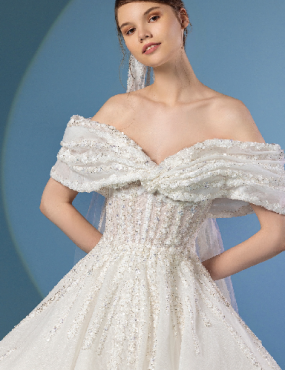 Woman in off-the-shoulder white wedding dress, sequins, soft veil, blue background.