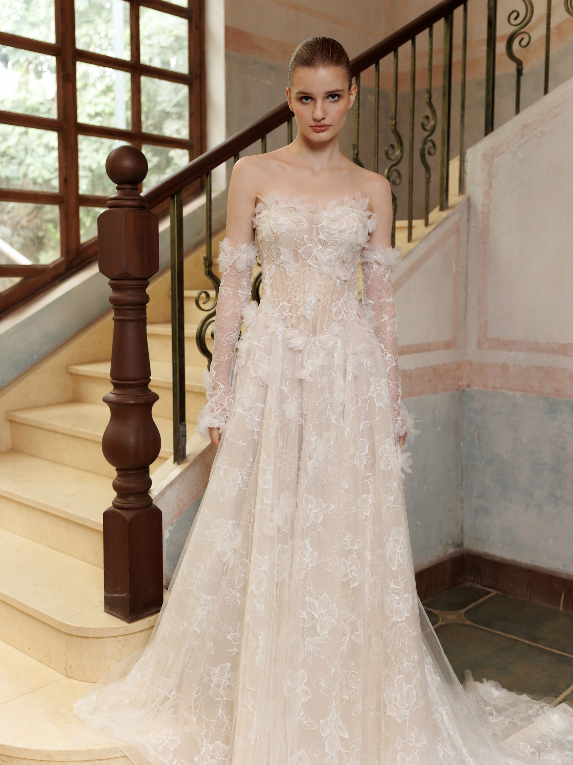 Woman in a strapless pale pink gown standing on a staircase with a floral, beaded train.