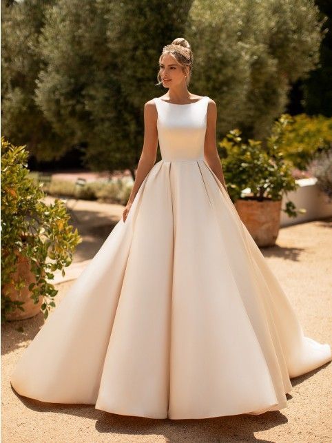 Woman in a white ball gown standing outdoors in a sunlit garden
