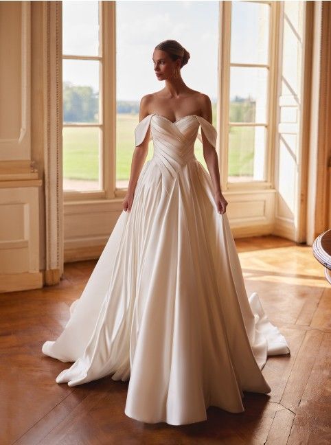 Bridal gown with long train displayed in a sunlit room with large windows and wooden floors