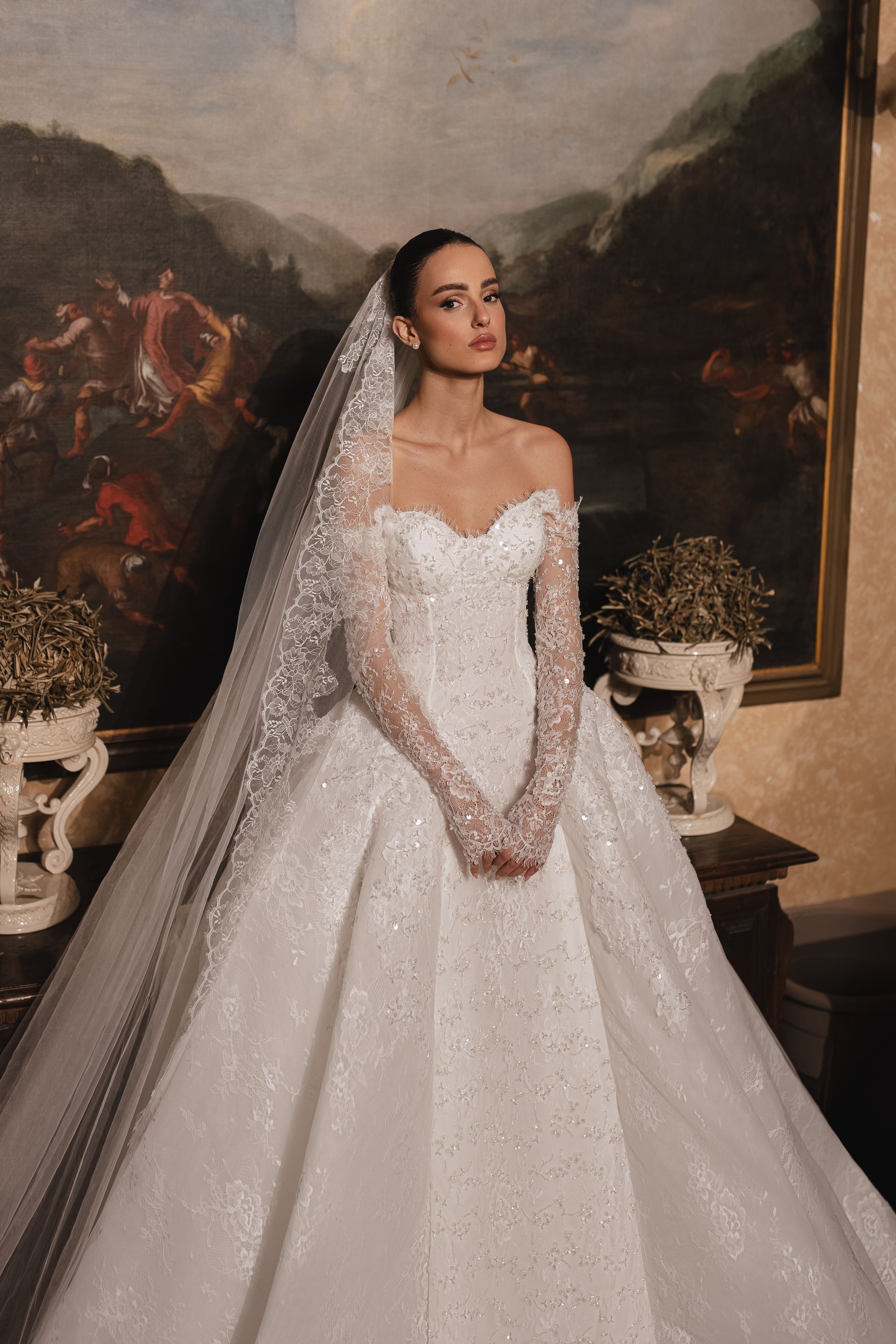 Woman in a white lace wedding gown on a stone staircase overlooking the ocean.