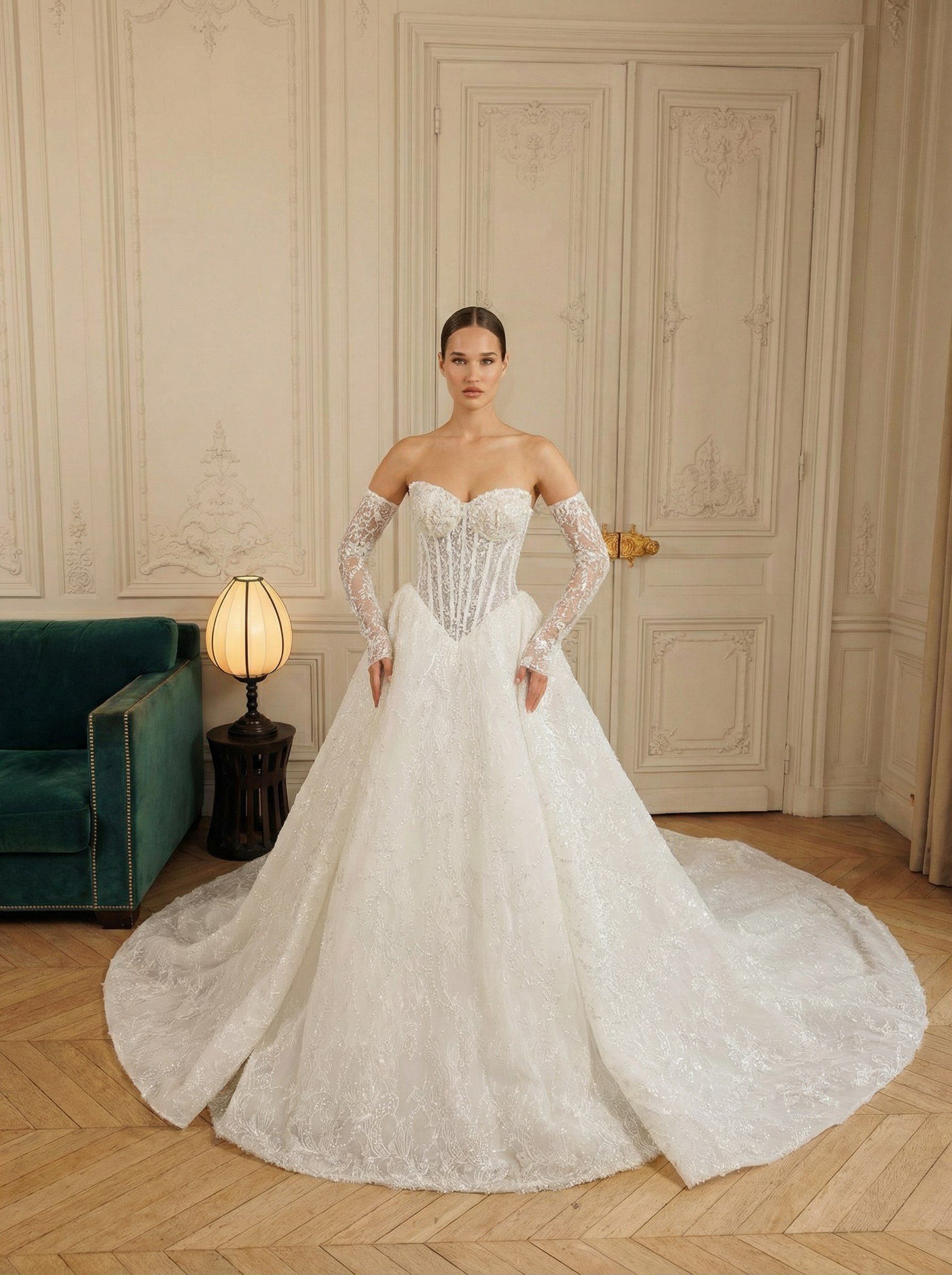 Woman in a white lace ball gown standing in an elegant room with paneled walls and a teal sofa